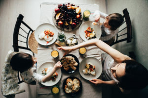 Aerial photo of two children eating breakfast with their mother. A fourth plate is set at the table but no one occupies its seat.