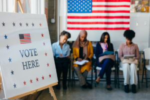 Photo of four women sitting down in line to vote.