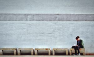 A young man sits alone on a bench while reading a book.