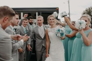 Just-married couple gets off a party bus while bridal party celebrates them